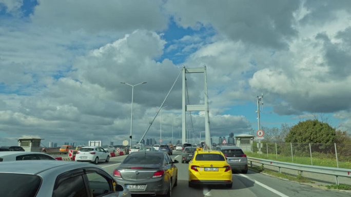 在晴朗的一天，土耳其伊斯坦布尔，车辆在高高的博斯普鲁斯大桥上移动，头顶多云的天空