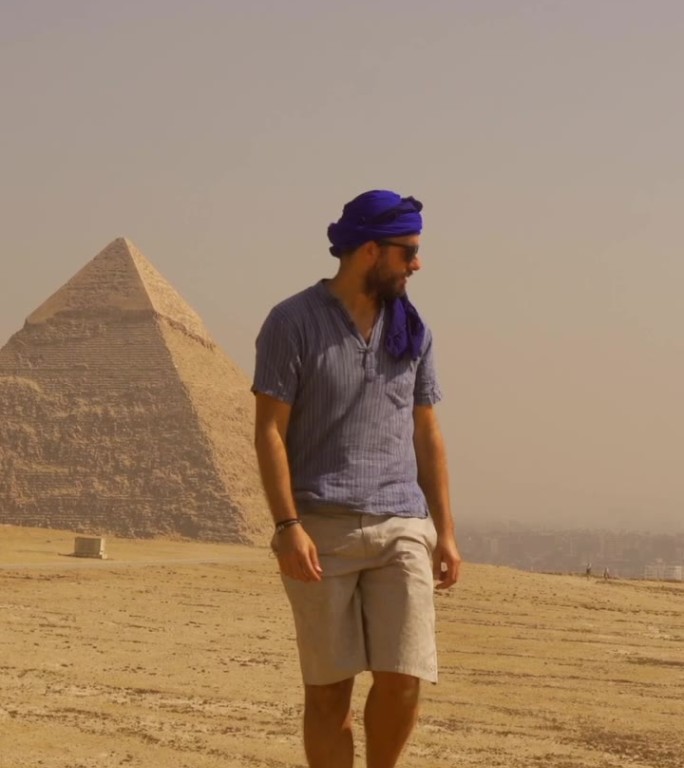 一个年轻的游客穿着蓝色的衣服，戴着头巾，走在吉萨金字塔旁边。开罗,埃及