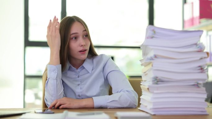 紧张的年轻女商人坐在桌子前，用电脑储存纸质文件