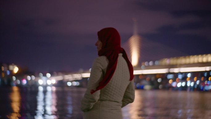 在金角海峡的博斯普鲁斯海峡上，女子为灯火通明的桥梁和城市灯光感到高兴。穆斯林的女人。