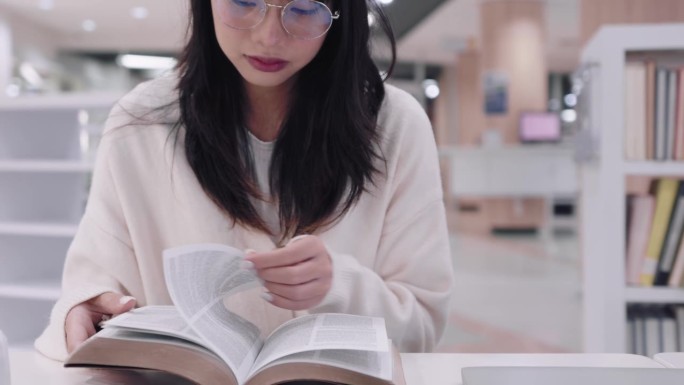 年轻的亚洲女大学生沉浸在学习中，阅读书籍研究和探索额外的课程，在大学图书馆准备考试。他们专注于学术探