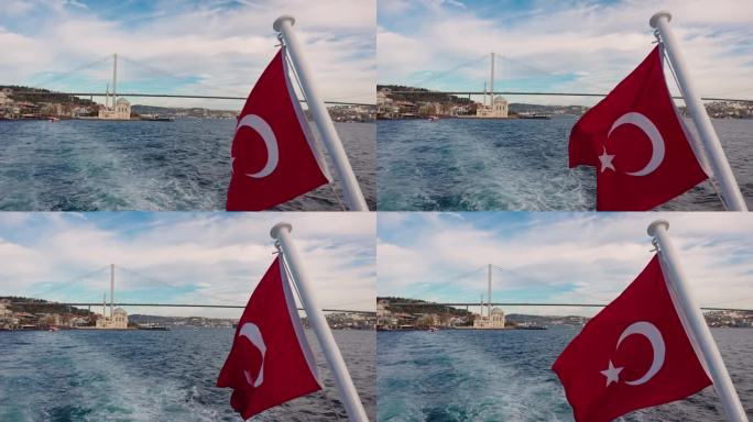 船的POV土耳其国旗在海上与Ortakoy清真寺和博斯普鲁斯桥在多云的天空背景