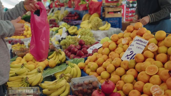 土耳其伊斯坦布尔，一名妇女手持相机从摊贩手中购买水果