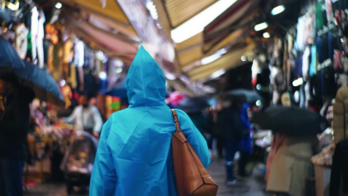 在土耳其伊斯坦布尔的服装市场，一名女子穿着雨衣，拿着钱包走在街上