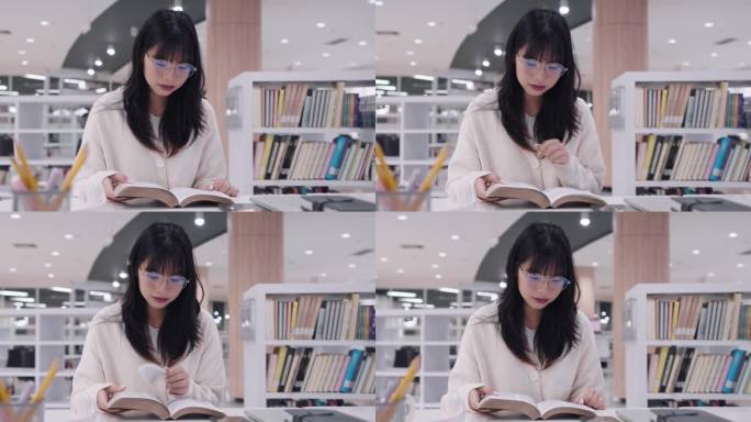 年轻的亚洲女大学生沉浸在学习中，阅读书籍研究和探索额外的课程，在大学图书馆准备考试。他们专注于学术探