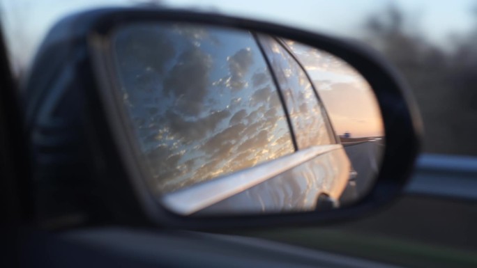 晚霞映照在行驶中的汽车后视镜上。近距离拍摄，实时拍摄，没有人