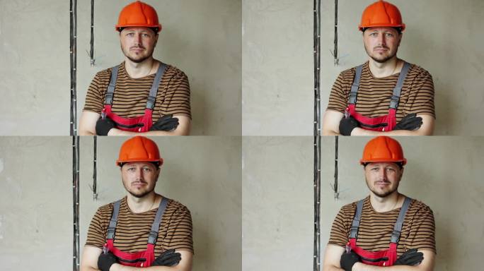 装修公寓。成熟自信的男性工头建筑修理工的肖像，双手交叉，戴着安全安全帽，穿着工作服，看着镜头，拿着螺