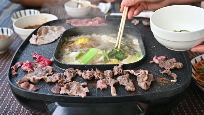 人们享受韩国烧烤和涮锅涮锅晚餐的派对画面。