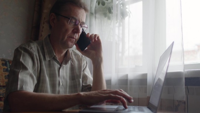 一个老人一边用智能手机打电话，一边用笔记本电脑打字。防止欺诈的概念。
