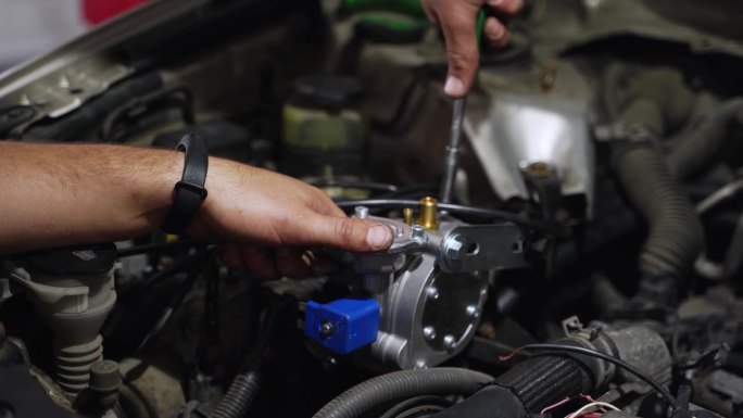 汽车修理工在汽车发动机上安装LPG减速器汽化器。手动固定用于气体转换的低压调节器。顺序多点液化石油气