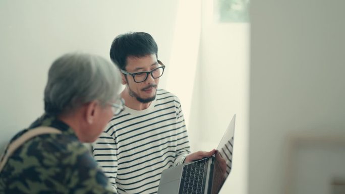 几代人的联系:亚洲男人在家工作，与他的长辈分享微笑和交谈。