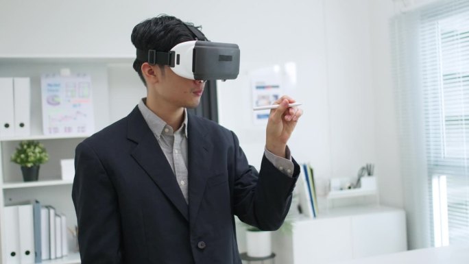 亚洲商人在现代办公室中使用虚拟现实视觉耳机与数据图形模拟来规划工作