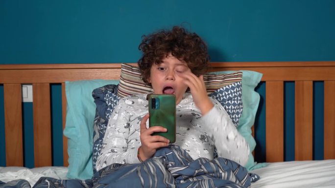9岁男孩带着智能手机上床睡觉——童年时期的疲劳和对社交媒体和互联网的沉迷——睡前看互联网是一个坏习惯