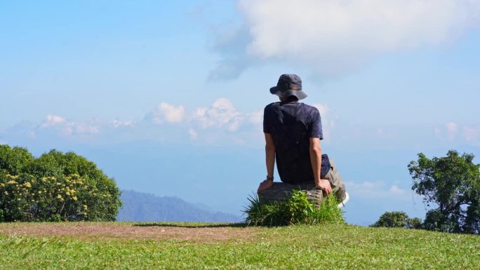 景观和旅行的概念与单独的自由职业者男人坐在木头上，从户外与山的背景层放松