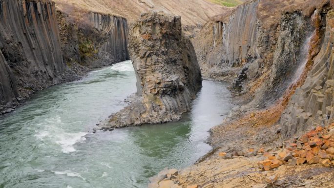 湍急的河流流经一个引人注目的冰岛峡谷，这里有独特的玄武岩柱状地层和崎岖的地形，展示了大自然的力量