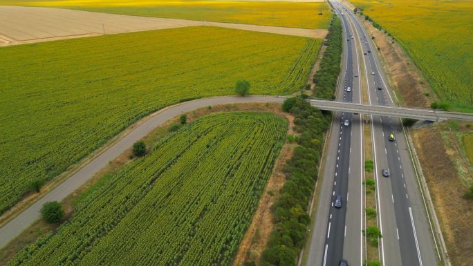 4K鸟瞰图，绿色农田之间的城际道路与快速行驶的汽车。无人机对高速公路交通的俯视图。
