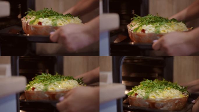 一个女人拿着烤盘，把烤盘和千层面放在烤箱里。烤宽面条，用新鲜的芝麻菜叶装饰，放在玻璃烤盘里。特写镜头