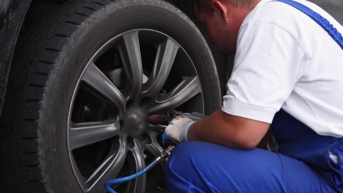 汽车修理工使用空气千斤顶抬起汽车，用气动螺母流道有效地去除轮胎。专业服务，车轮保养。车间维修工作在快