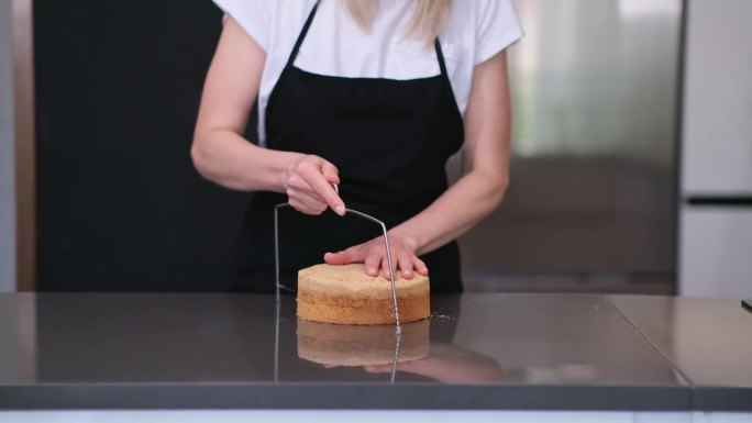 穿着黑色围裙的金发糖果师站在现代厨房里切着烤好的面团