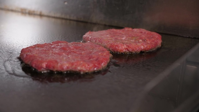 餐厅厨房里煎的两个肉汉堡的特写。