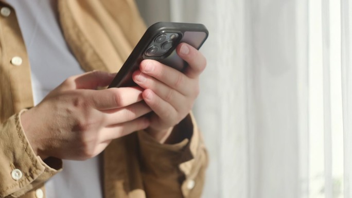 女性的手近距离使用智能手机浏览，站在家里的窗口附近的设备上上网。点击按钮，点击链接。早上打电话。技术
