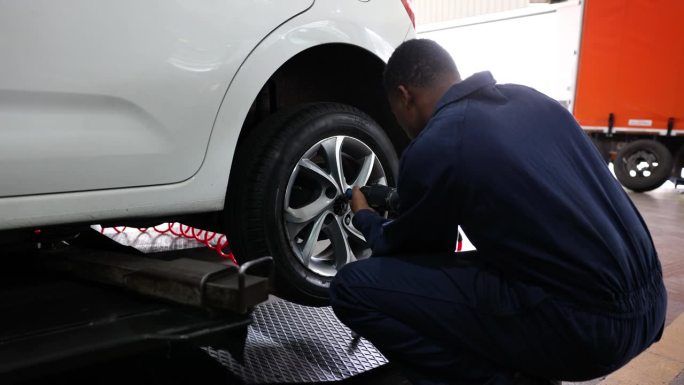 在一家汽车修理店，一名黑人男修理工正在把漏气的轮胎从车上卸下来修理