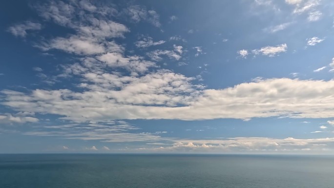 在平静的海面上，蓝色的夏日天空中飘动着飘忽的蓬松积云。抽象的空中自然夏季海洋日落，大海和天空的看法。