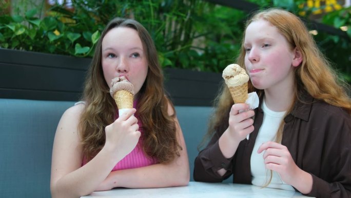 青少年，两个女孩，朋友，在购物中心的公园里吃冰淇淋，红头发，白皙的皮肤，夏天的交流，会议，冰淇淋甜筒