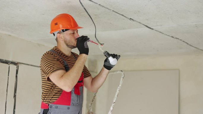 电工制服，防护手套和安全帽，用测试螺丝刀检查和测量灯泡电压。用电压检测仪检测新楼电线