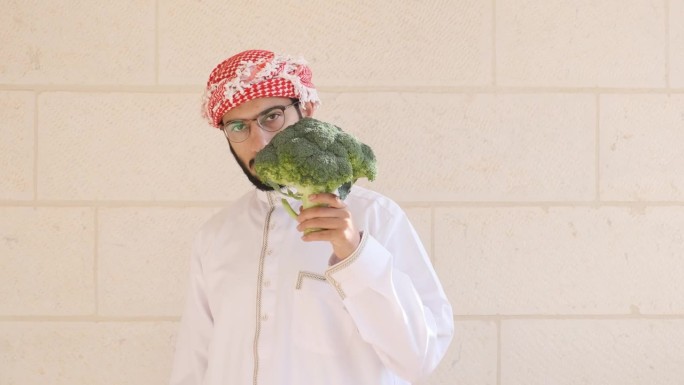 阿拉伯男子拿着花椰菜，脸上带着微笑，以一种有趣的方式讲述着吃蔬菜的好处