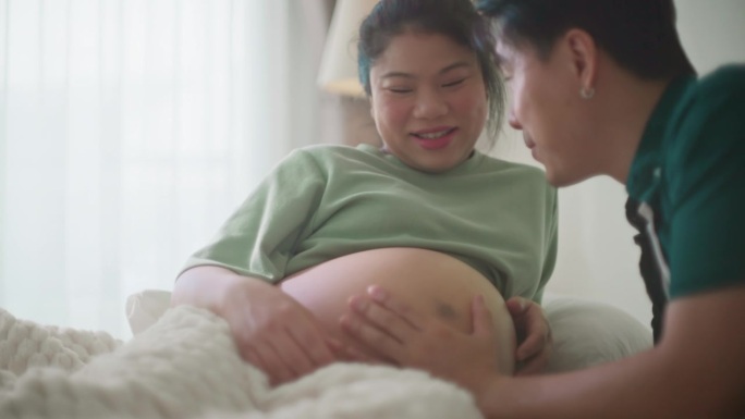 亚洲已婚丈夫对他怀孕的妻子倾注爱意，在她成长的肚子上播种一个充满爱的吻，在家里听着他婴儿般的心跳声
