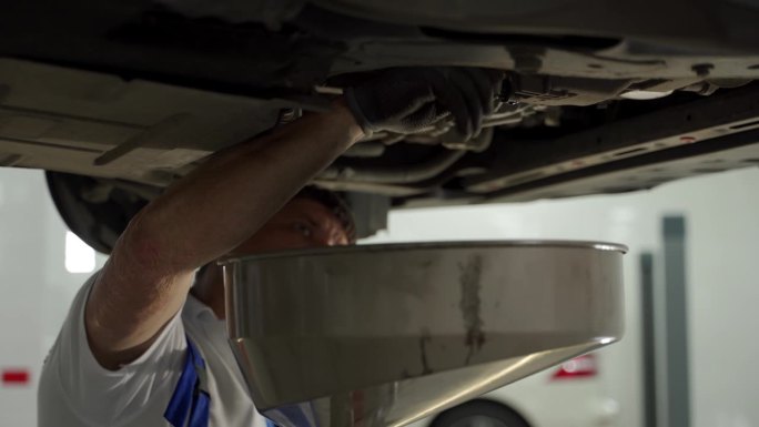 汽车修理工在日常保养时把车里的旧油放掉。专业从事车库更换润滑油，车辆吊装，车间环境。亲自操作换油程序