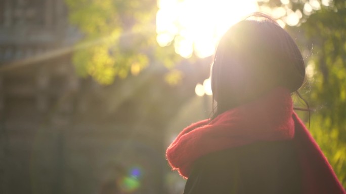 一个戴红色围巾的女人站在阳光下看远方风景