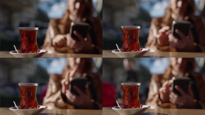 土耳其伊斯坦布尔，一名女子坐在路边咖啡馆边喝红茶边使用智能手机