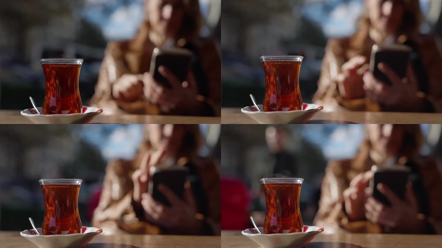 土耳其伊斯坦布尔，一名女子坐在路边咖啡馆边喝红茶边使用智能手机