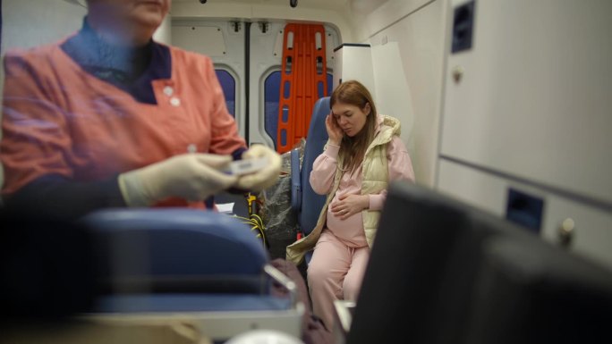 一名年轻的怀孕女孩在救护车里感到焦虑，她一直在抚摸自己的肚子，安慰自己和未出生的婴儿。