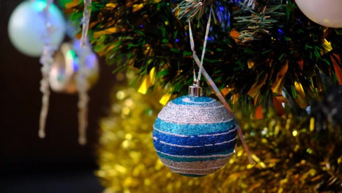 凑近一棵圣诞树，灯火在夜晚闪闪发光。包厢里装饰。圣诞树的树枝上有明亮的球，背景是模糊的闪闪发光的仙女