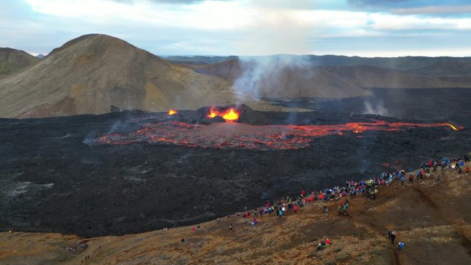 火山喷发的空中移动镜头。人们站在离火山和热熔岩安全距离的地方。游客们来看从地下流出的岩浆。一生的经历