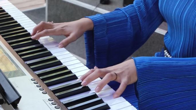 年轻女子在户外弹奏数字钢琴。在城市市场举办小型音乐会。穿着电蓝色连衣裙的女人。