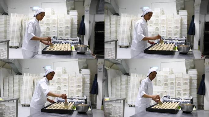 非裔美国女面包师在一家工业面包店用蛋液刷牛角面包