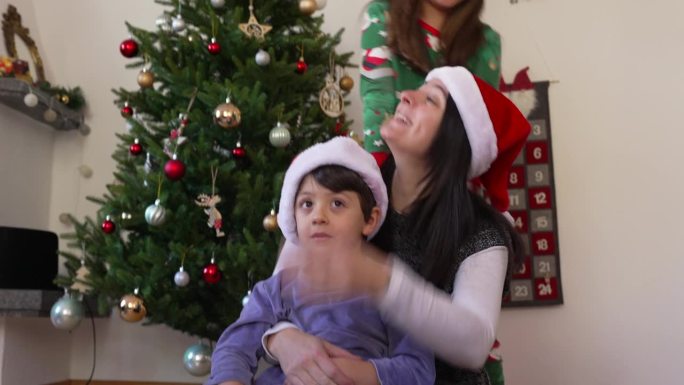 母亲与孩子合影的全家福，以圣诞树为背景。妈妈和儿子戴着红色的帽子，坦率而真实的童年记忆