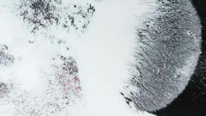 蓬松的大刷子从透明的表面上擦去雪或白色粉末，从下面拍摄