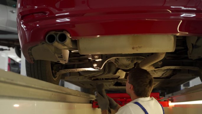 汽车修理工用液压探测仪检查车底悬挂转向系统。专业使用远程检查车辆安全，维修工作在车库。正在使用的诊断