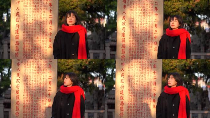 一个戴红色围巾的女人站在石碑阳光下看远方