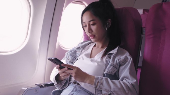 目前，乘坐飞机旅行的亚洲女性正愉快地戴着耳机听音乐，轻声哼唱。能唤起快乐和放松