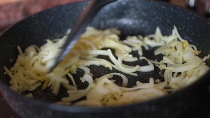 妇女在炉子上的煎锅里煮洋葱(特写)