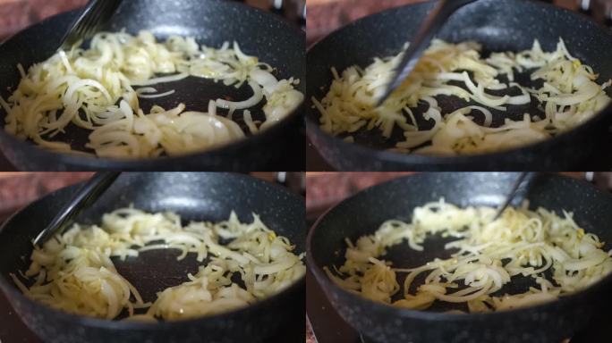 妇女在炉子上的煎锅里煮洋葱(特写)