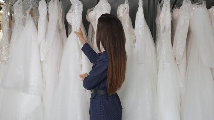 一位年轻美丽的女子在婚礼沙龙里挑选婚纱。