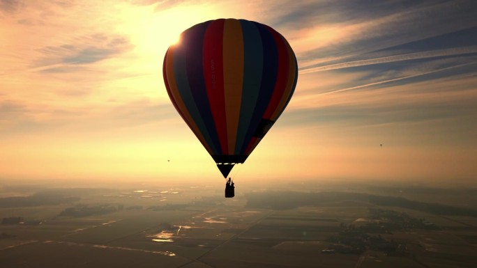 在夕阳下的乡村，无人驾驶飞机绕着橙色天空下的彩色热气球飞行