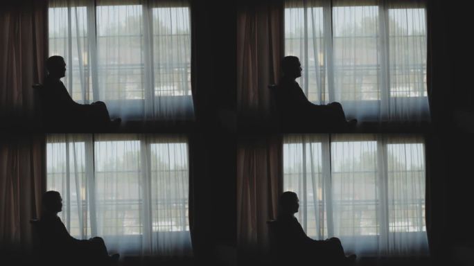 窗边有个人影。穿着经典西装的人坐在靠窗的椅子上，慢镜头。